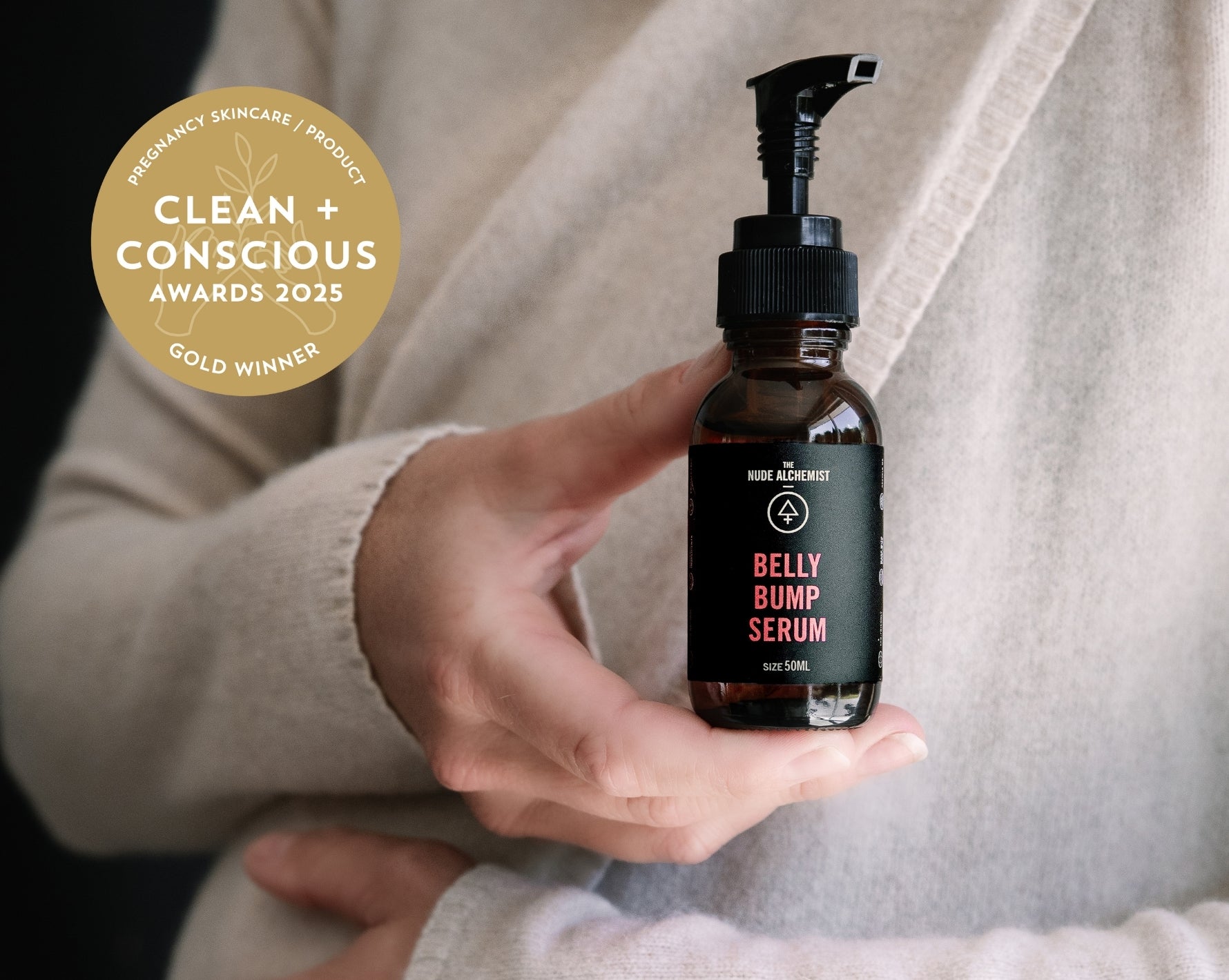 Bottle of 'Belly Bump Serum' held in a hand with 'Clean + Conscious Awards 2023' gold winner badge. the nude alchemist stretch mark oil