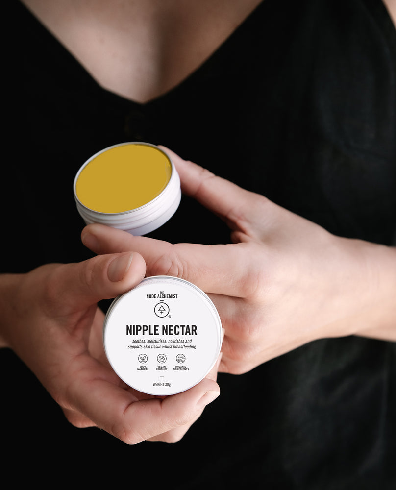 Person holding an open tin of Nipple Nectar balm, a breastfeeding aid to soothe and support skin tissue