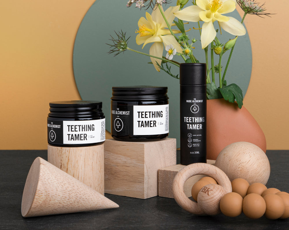 Product shot of all three variants of Teething Tamer on wooden blocks with plants in the background. 