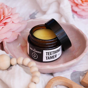 Product shot of Teething Tamer 30g glass jar resting on pink and wooden toned background.